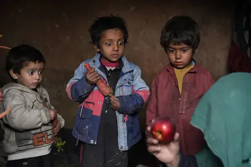 Three internally displaced children look with surprise at an apple that their mother brought home after begging, in a camp on the outskirts of Kabul, Afghanistan, Thursday, Feb 2, 2023. Since the chaotic Taliban takeover of Kabul on Aug. 15, 2021, an already war-devastated economy once kept alive by international donations alone is now on the verge of collapse. (AP Photo/Ebrahim Noroozi)