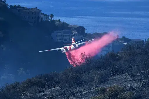 A plane drops retardant on a wildfire near homes Thursday, Feb. 10, 2022, in Laguna Beach, Calif. U.S. officials are testing a new wildfire retardant after two decades of buying millions of gallons annually from one supplier, but watchdogs say the expensive strategy is overly fixated on aerial attacks at the expense of hiring more fire-line digging ground crews.  (AP Photo/Ringo H.W. Chiu, File)