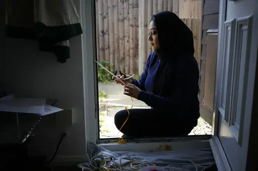 Bilqis Alam, an energy advisor from the South East London Community Energy co-operative (Selce), installs draught proofing rubber strips to the front door frame of the home of her client Tia Rutherford, in south east London, Tuesday, March 22, 2022. People across the United Kingdom will face tough choices in coming months as energy costs for millions of households are set to rise by 54% on Friday. It's the second big jump in energy bills since October, and a third may be ahead as rebounding dema