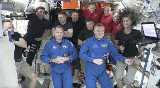 In this image made from a NASA livestream, the two astronauts stuck at the International Space Station since June 2024, Butch Wilmore, far left, and Suni Williams, far right, welcome two new residents who flew up on SpaceX, NASA's Nick Hague, front left in blue, and the Russian Space Agency's Alexander Gorbunov, front right in blue, Sunday, Sept. 29, 2024. Behind them, from left in black, are NASA's Jeanette Epps, Russia's Alexander Grebenkin, NASA's Mike Barratt and NASA's Matthew Dominick. Fro