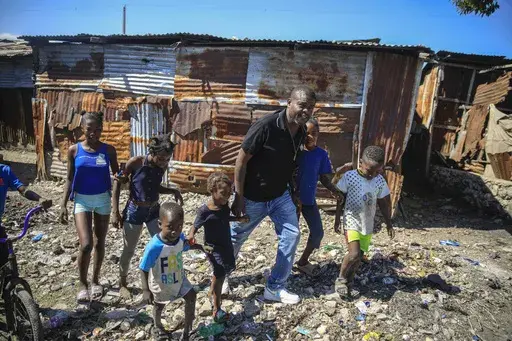 Jimmy Cherizier, a former elite police officer known as Barbecue who now runs a gang federation, walks hand in hand with children as he visits La Saline district of Port-au-Prince, Haiti, Jan. 24, 2023. Internationally, Cherizier is known as Haiti's most powerful and feared gang leader, sanctioned by the United Nations for "serious human rights abuses," and the man behind a fuel blockade that brought the Caribbean nation to its knees in late 2022. (AP Photo/Odelyn Joseph, File)