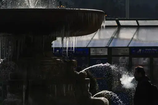 A pedestrian walks past a partially frozen fountain in New York, Tuesday, Jan. 11, 2022. A mass of arctic air swept into the Northeast on Tuesday, bringing bone-chilling sub-zero temperatures and closing schools across the region for the second time in less than a week. (AP Photo/Seth Wenig)