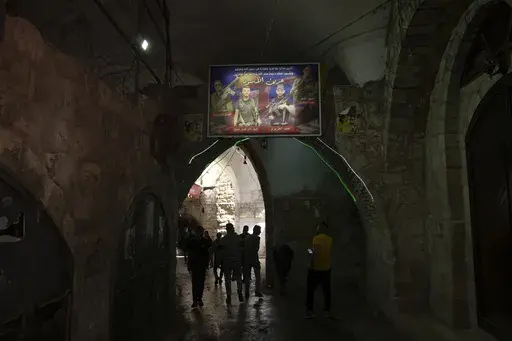 Palestinians walk under a banner depicting militants from the Lions' Den group who were killed by Israeli forces, from left, Fadi Qufesheh, Abdulrahman Soboh, Mohammad Azizi and Mahmoud Zakari, in al-Yasmeena quarter of the Old City of Nablus, in the West Bank, Thursday, May 4, 2023. The killing of Zuhair al-Ghaleeth last month, the first slaying of a suspected Israeli intelligence collaborator in the West Bank in nearly two decades, has laid bare the weakness of the Palestinian Authority and th