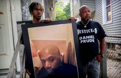 Armin Prude, left, and Joe Prude hold an enlarged photo of Daniel Prude, Sept. 3, 2020, who died following a police encounter, in Rochester, N.Y. City officials have agreed to pay $12-million to the family of Daniel Prude, a Black man who died after police held him down until he stopped breathing after encountering him running naked through the snowy streets of Rochester, NY. A federal judge approved the settlement in a court document filed Thursday, Oct. 6, 2022. (AP Photo/Ted Shaffrey, File)