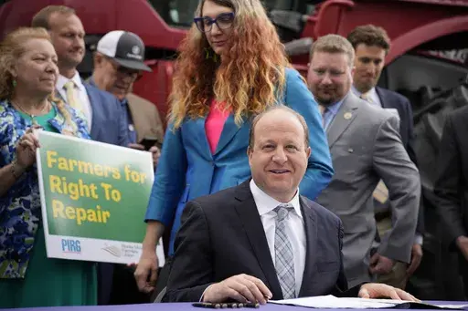 Colorado Gov. Jared Polis, front, waits to sign legislation that forces manufacturers to provide the necessary manuals, tools, parts and even software to farmers so they can fix their own machines, Tuesday, April 25, 2023, during a ceremony outside the State Capitol in Denver. Colorado is the first state to put the right-to-repair law into effect while at least 10 other states are considering similar measures. Colorado State Rep. Brianne Titone, center, and Rep. Ron Weinberg, back, head in to wi