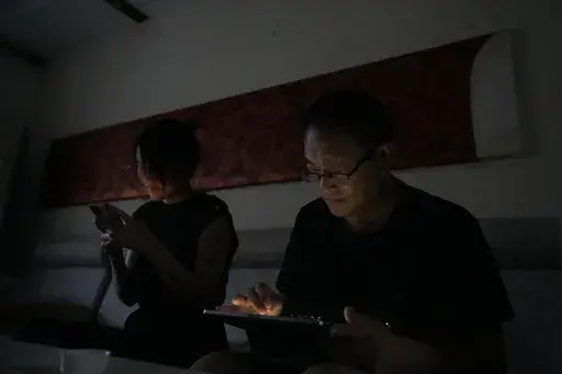 Wang Quanzhang and his wife Li Wenzu look at their phone and laptop in the dark after power was cut off for their apartment in Beijing's Changping district, Tuesday, June 20, 2023. Disbarred human rights lawyer Wang Quanzhang has been forced to move 13 times in two months as part of a pattern of harassment against him and three other prominent rights advocates in Beijing that is further squeezing the country's battered civil rights community. (AP Photo/Ng Han Guan)