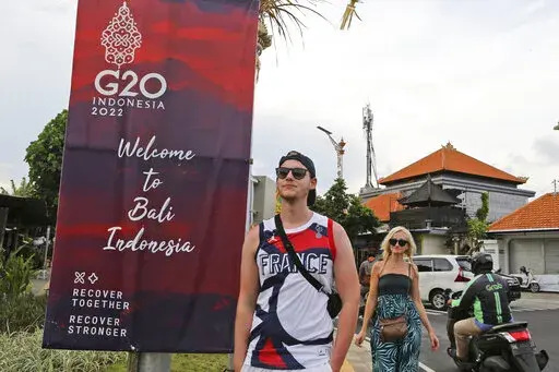 Tourists walk past a G20 banner in Nusa Dua, Bali, Indonesia on Friday, Nov. 11, 2022. The dozens of world leaders and other dignitaries traveling to Bali for the G-20 summit will be drawing a welcome spotlight on the revival of the tropical island's ailing tourism sector after a two-year closure to foreign travelers due to the pandemic. (AP Photo/Firdia Lisnawati)