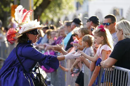 A woman dressed in period costume hands a trinket to a child during a parade dubbed "Tardy Gras," to compensate for a cancelled Mardi Gras due to the COVID-19 pandemic, in Mobile, Ala., on May 21, 2021. Mobile, Alabama’s first big parade of the Mardi Gras season is scheduled for Friday night. (AP Photo/Gerald Herbert, File)
