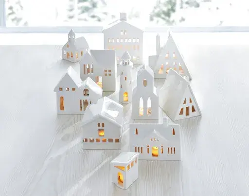 This image provided by Crate & Barrel shows their collection of white ceramic buildings. Crate & Barrel's collection includes alpine homes and hotels as well as midcentury split levels and ranch homes. Add a tealight for a welcoming glow. (Crate & Barrel via AP)