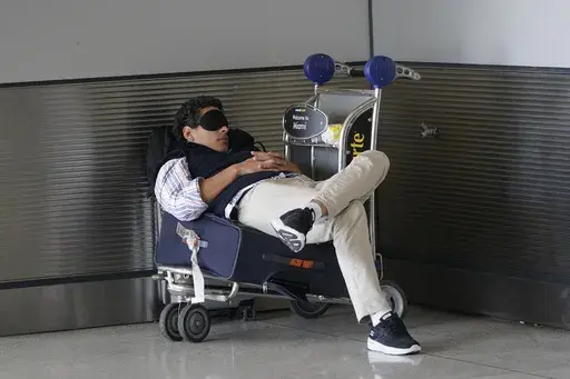 A traveler takes a nap as he waits for a ride outside Miami International Airport, Friday, July 1, 2022, in Miami. The Gallup survey, released Monday, April 15, 2024, says that a majority of Americans say they would feel better if they could have more sleep. But in the U.S., where the ethos of grinding and pulling yourself up by your own bootstraps is ubiquitous, getting enough sleep can seem like a dream. (AP Photo/Wilfredo Lee, File)