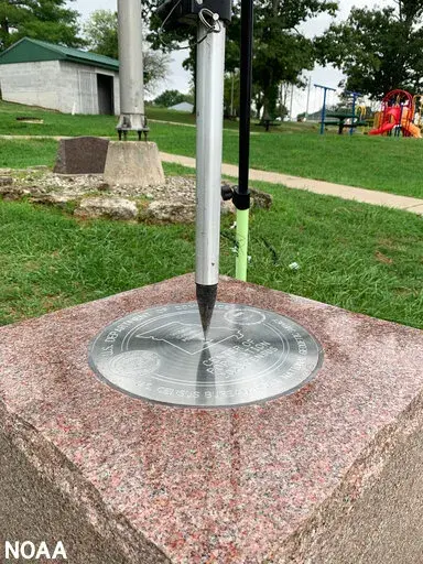 This photo provided by NOAA shows the tip of a tripod resting on the center of the 2020 Center of Population Commemorative Survey mark, as part of a GPS survey to determine the precise latitude, longitude, and height of the mark on Sept. 14, 2022 in Hartville, Mo.  The U.S. Census Bureau announced the nation’s new center of population in 2020 to be in Hartville, in the Ozark Mountains.  (NOAA via AP)