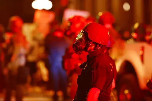 FILE -A Denver Police officer wears a gas mask before tear gas and rubber bullets were used to disperse protesters outside the State Capitol over the death of George Floyd, Thursday, May 28, 2020, in Denver. A federal jury’s $14 million award to Denver protesters injured during 2020 demonstrations over the killing of George Floyd could resonate nationwide as courts weigh more than two dozen similar lawsuits.(AP Photo/David Zalubowski, File)