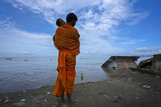 Ranajit Mandal, 35, the priest of a temple of Hindu goddess Durga stands with his son watching the temple being washed away by the river Brahmaputra at Murkata village, northeastern Assam state, India, Thursday, Oct. 13, 2022. "The river has washed away everything, and we have no place to go back to now," he said. "Even though we are staying nearby now, if this continues, we'll have no choice but to move away from here, away from the river." (AP Photo/Anupam Nath)