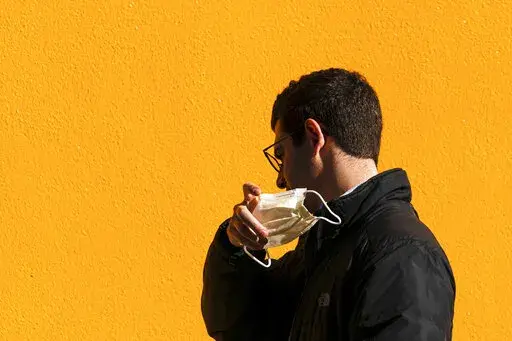 A pedestrian removes a protective mask worn as a precaution against the spread of the coronavirus in Philadelphia, Wednesday, March 2, 2022. People in Philadelphia could be excused if they felt a sense of whiplash Friday, April 22, 2022 as the city abandoned its indoor mask mandate just days after becoming the first big U.S. city to reimpose compulsory masking in response to an increase in COVID-19 cases and hospitalizations. (AP Photo/Matt Rourke, File)