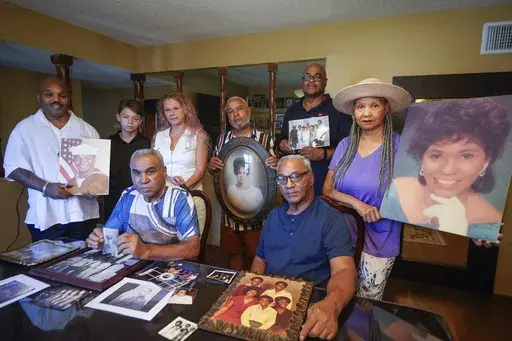 Descendants of Nelson Bell, brothers Milford Fonza, front left, and Elmer Fonza, front right, surrounded by extended family members, show their ancestors' pictures in Glendora, Calif., on Friday, Sept. 8, 2023. Family members standing from left: Trent Mure, with son Armani Mure, and his wife Tami Mure, William Woolery, Louie Hobbs and Carolyn Fonza. (AP Photo/Damian Dovarganes)