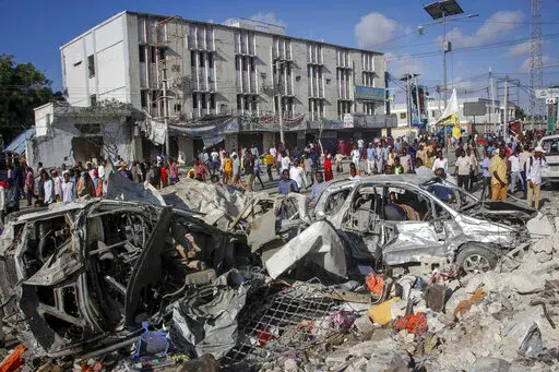 People walk amidst destruction at the scene, a day after a double car bomb attack at a busy junction in Mogadishu, Somalia Sunday, Oct. 30, 2022. Somalia's president says multiple people were killed in Saturday's attacks and the toll could rise in the country's deadliest attack since a truck bombing at the same spot five years ago killed more than 500. (AP Photo/Farah Abdi Warsameh)