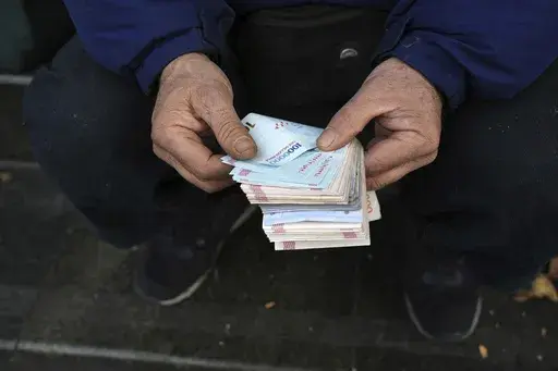 A street money exchanger poses for a photo without showing his face as he counts Iranian banknotes at a commercial district in downtown Tehran, Iran, Friday, Dec. 23, 2022. Iran’s currency fell to a record low on Sunday, plunging to 613,500 to the dollar, as its people celebrated the Persian New Year. (AP Photo/Vahid Salemi, File)
