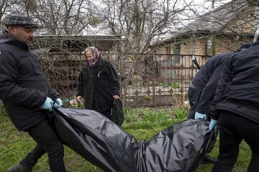 Vlad Minchenko, left, carries a plastic bag with the dead body of Stanislav Berestnev who died during the Russian occupation and was buried in the graveyard in Bucha, Ukraine, Tuesday, April 19, 2022. Minchenko wakes every day with trembling hands. For hours, until it eases, he can't message on his phone or even consider his previous work of making art or tattoos. But he can continue to retrieve bodies, scores of bodies, around the Ukrainian town of Bucha as part of a task that continues more th