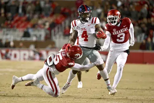 Mississippi running back Quinshon Judkins (4) is tackled by Arkansas defenders Simeon Blair (15) and Dwight McGlothern (3) during the first half of an NCAA college football game Saturday, Nov. 19, 2022, in Fayetteville, Ark. (AP Photo/Michael Woods)