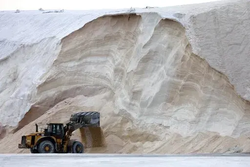A front-end loader works in front of a pile of road salt, Friday, Jan. 28, 2022, in Chelsea, Mass. Residents and officials in the Northeast and mid-Atlantic regions of the U.S. are bracing for a powerful winter storm expected to produce blizzard conditions Friday and Saturday. (AP Photo/Michael Dwyer)