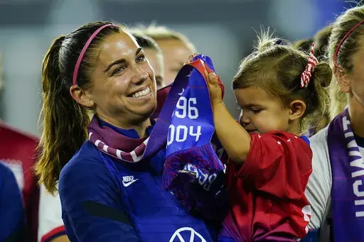 FILE -United States' Alex Morgan holds her daughter, Charlie, as she listens to Cindy Parlow Cone, president of the U.S. Soccer Federation, speak during an event with the federation, U.S. Women's National Team Players Association and the U.S. National Soccer Team Players Association at Audi Field in Washington, Tuesday, Sept. 6, 2022. Morgan says she feels calmer heading into this World Cup and wants to represent mom athletes. She's one of three mothers on this U.S. squad and is often accompanie