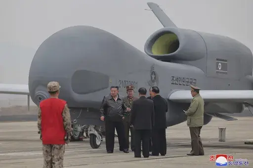 In this photo provided Thursday, March 27, 2025, by the North Korean government, its leader Kim Jong Un, center left in a black jacket, stands by what appeared to be a large reconnaissance drone at an undisclosed location in North Korea, earlier this week. Independent journalists were not given access to cover the event depicted in this image distributed by the North Korean government. The content of this image is as provided and cannot be independently verified. Korean language watermark on ima