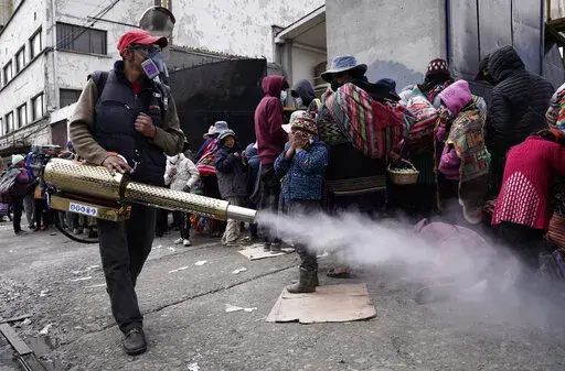 A worker sprays disinfectant around people who traveled from the provinces to Monte de Oración church for donated food and clothing during the church's annual Good Samaritan campaign in La Paz, Bolivia, Tuesday, Dec. 28, 2021. Due to the COVID-19 pandemic, the church is distributing the goods outdoors. (AP Photo/Freddy Barragan)