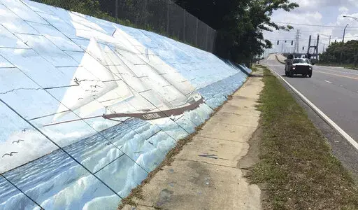 Traffic passes a mural of the slave ship Clotilda along Africatown Boulevard, in Mobile, Ala., May 30, 2019. Republican Tommy Tuberville told people Saturday, Oct. 8, 2022, at an election rally in Nevada that Democrats support reparations for the descendants of enslaved people because “they think the people that do the crime are owed that.” His remarks cut deeply for some, especially in and around Africatown, a community in Mobile, Alabama, that was founded by descendants of Africans smuggle