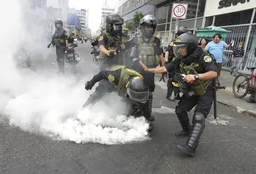 Police officers pick up a tear gas canister that was thrown back at them by anti-government protesters who traveled to the capital from across the country to march against Peruvian President Dina Boluarte in Lima, Peru, Wednesday, Jan. 18, 2023. Protesters are seeking immediate elections, Boluarte's resignation, the release of ousted President Pedro Castillo and justice for the dozens of protesters killed in clashes with police. (AP Photo/Martin Mejia)