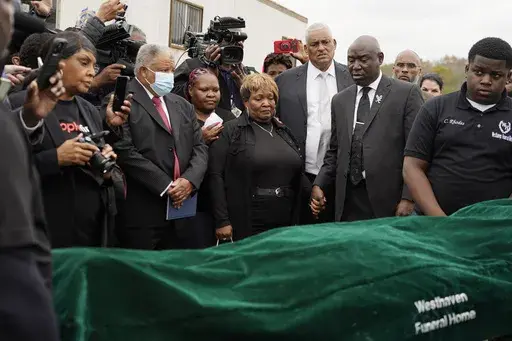 Surrounded by family members and holding hands with civil rights attorney Ben Crump, center right, Bettersten Wade, center, mother of Dexter Wade, a 37-year-old man who died after being hit by a Jackson, Miss., police SUV driven by an off-duty officer, watches her son's body transferred to a mortuary transport in Raymond, Miss. Nov. 13, 2023. An independent pathologist says the deceased Mississippi man had a wallet in the front pocket of the jeans he was buried in that contained his home address