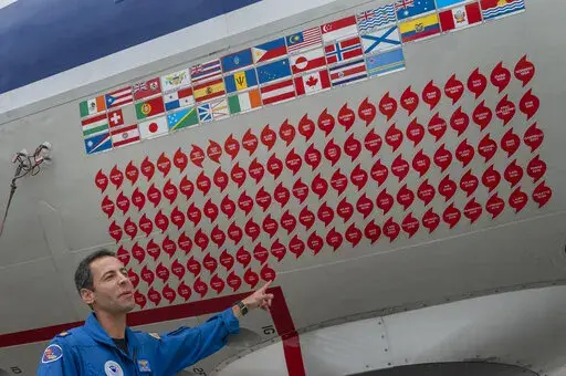 Lt. Commander Sam Urato, a P-3 pilot of National Oceanic and Atmospheric Administration, points to decals on the fuselage of the Lockheed WP-3D Orion 'hurricane hunter' aircraft representing the hurricanes it has penetrated during a hurricane awareness tour at Washington National Airport, Arlington, Va., Tuesday, May 3, 2022. Hurricane season starts Wednesday, June 1, 2022, and it's looking busy because every factor out there is pointing to another nasty year in the Atlantic. (AP Photo/Gemunu Am