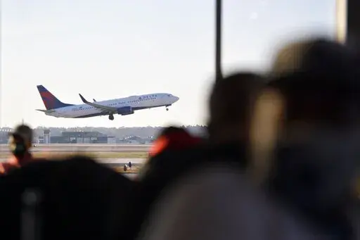 A Delta Airlines aircraft takes off as passengers await the boarding process, Thursday, Dec. 2, 2021, at Hartsfield-Jackson Atlanta International Airport, in Atlanta.  For another year, summer travel plans are up in the air even as more people are ready to take to the skies. Summer vacations are roaring back, but you still need Plans A, B and possibly C to make sure you get away. Book flights and lodging early and take advantage of more generous change and cancellation policies. If traveling int