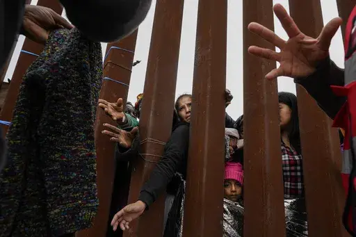 Migrants reach through a border wall for clothing handed out by volunteers as they wait between two border walls to apply for asylum Friday, May 12, 2023, in San Diego. Hundreds of migrants remain waiting between the two walls, many for days. The image was part of a series by Associated Press photographers Ivan Valencia, Eduardo Verdugo, Felix Marquez, Marco Ugarte Fernando Llano, Eric Gay, Gregory Bull and Christian Chavez that won the 2024 Pulitzer Prize for feature photography. (AP Photo/Greg