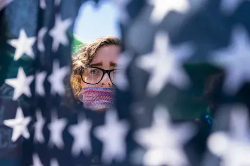 Emma Rousseau of Oakland, N.J., her mouth bound with a red, white and blue netting, attends a rally on the Fourth of July to protest for abortion rights, at Lafayette Park in front of the White House in Washington, Monday, July 4, 2022. One year ago, the U.S. Supreme Court rescinded a five-decade-old right to abortion, prompting a seismic shift in debates about politics, values, freedom and fairness. (AP Photo/Andrew Harnik, File)