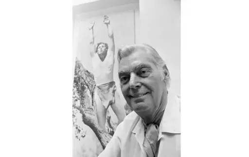 Olympic hero and film actor Johnny Weissmuller is pictured in front of a photo of himself as Tarzan, June 29, 1971. Weissmuller, who played Tarzan in the films was a swimming superstar in France 100 years ago. (AP Photo, File)