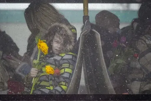 A refugee child fleeing the conflict from neighbouring Ukraine holds flowers, given out to celebrate International Women's Day, as he sits on a bus, at the Romanian-Ukrainian border, in Siret, Romania, Tuesday, March 8, 2022. It is a global day to celebrate women, but many fleeing Ukraine feel only the stress of finding a new life for their children as husbands, brothers and fathers stay behind to defend their country from Russia's invasion. (AP Photo/Andreea Alexandru)