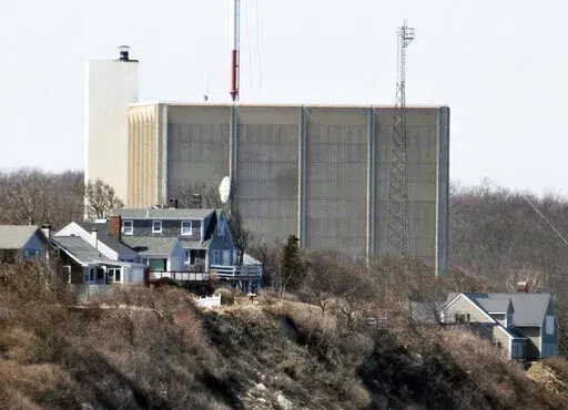 A portion of the Pilgrim Nuclear Power Station is visible beyond houses along the coast of Cape Cod Bay, in Plymouth, Mass., March 30, 2011. Pilgrim, which closed in 2019, was a boiling water reactor. Water constantly circulated through the reactor vessel and nuclear fuel, converting it to steam to spin the turbine. The water was cooled and recirculated, picking up radioactive contamination. (AP Photo/Steven Senne, File)