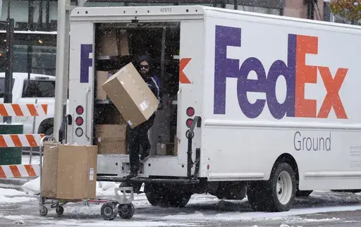 A FedEx delivery person carries a package from a truck on Nov. 17, 2022, in Denver. (AP Photo/David Zalubowski, File)