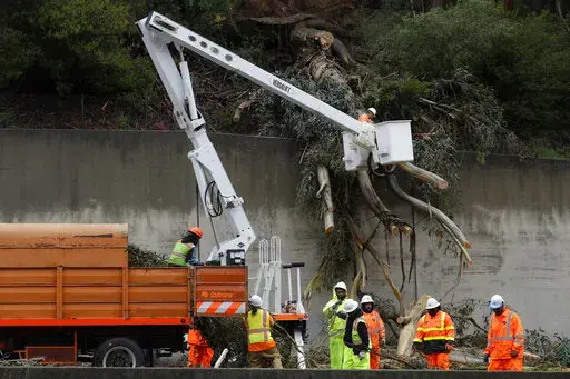 Caltrans workers clear the remains of a 100-foot eucalyptus tree from the northbound lanes of Highway 13 in Oakland, Calif., on Thursday, Dec. 23, 2021. Heavy overnight rains in Northern California left two people dead in a submerged car as authorities on Thursday urged residents of several Southern California mountain and canyon communities to voluntarily leave their homes because of possible mud and debris flows. (Jane Tyska/Bay Area News Group via AP)