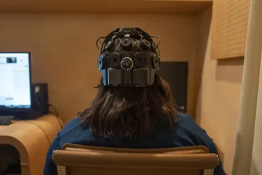Emily Hollenbeck, a deep brain stimulation therapy patient, demonstrates an EEG device that records brain activity as she reacts to short videos at Mount Sinai’s “Q-Lab” in New York on Dec. 20, 2023. Dr. Brian Kopell, who directs Mount Sinai's Center for Neuromodulation, says in normal brains electrical activity reverberates unimpeded in all areas, in a sort of dance. In depression, the dancers get stuck within the brain’s emotional circuitry. DBS seems to “unstick the circuit,” he s