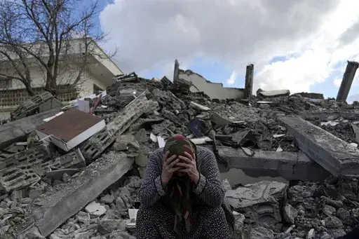A woman sits on the rubble as emergency rescue teams search for people under the remains of destroyed buildings in Nurdagi town on the outskirts of Osmaniye city southern Turkey, Feb. 7, 2023. A year after the devastating 7.8 magnitude earthquake struck southern Turkey and northwestern Syria, a massive rebuilding effort is still trudging along. The quake caused widespread destruction and the loss of over 59,000 lives. (AP Photo/Khalil Hamra, File)