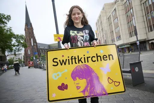 Schoolgirl Aleshanee Westhoff shows a "Swiftkirchen" town sign in honor of musician Taylor Swift in Gelsenkirchen, Germany, Tuesday, July 2, 2024. The Swifties are about to take over the German city of Gelsenkirchen, where American superstar Taylor Swift is set to give three concerts of her Eras Tour later this month. In honor of the singer, the city renamed itself “Swiftkirchen" — at least temporarily to welcome the tens of thousands of fans who are expected to come for the Eras Tour shows 