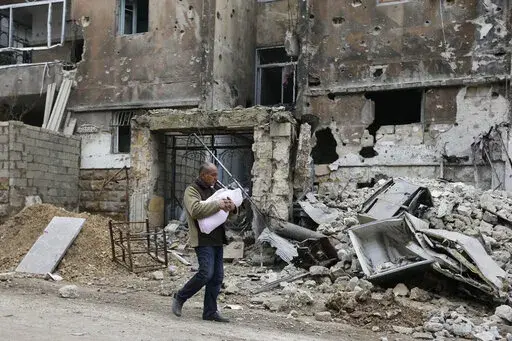 In this Jan. 20, 2017 photo, a man carries a baby as he walks past rubble in the once rebel-held Salaheddine neighborhood of eastern Aleppo, Syria. Tuesday, March 15, 2022 marks the 11th anniversary of Syria's revolution-turned-civil war. This year, many survivors are watching in shock as Ukrainians face the same horrors they did. (AP Photo/Hassan Ammar, File)