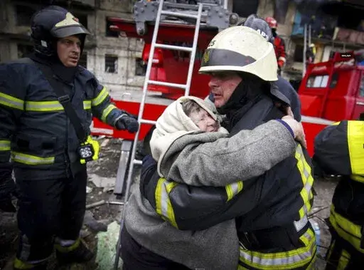 In this photo released by Ukrainian State Emergency Service, a firefighter hugs an elderly woman after evacuation from an apartment building hit by shelling in Kyiv, Ukraine, Monday, March 14, 2022. (Ukrainian State Emergency Service via AP)