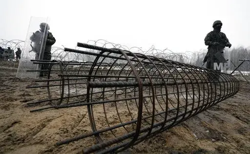 Guards and the military watching the start of work on the first part of a 180 kilometers (115 miles) and 5.5 meter (18ft)-high metal wall intended to block migrants from Belarus crossing illegally into EU territory, in Tolcze, near Kuznica, Poland, Jan. 27, 2022. When relations with Belarus deteriorated after its authoritarian President Alexander Lukashenko was declared the winner of an election widely seen as fraudulent, the government in Minsk sent thousands of migrants streaming across the EU