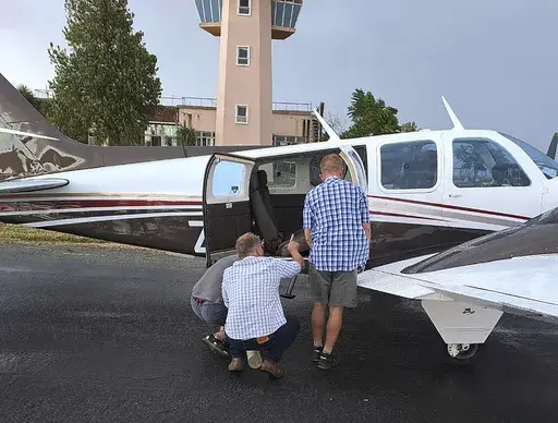 In this photo provided by Brian Emmenis, people look inside a plane at the Welkom Airport, in Welkom, South Africa, as they search for a venomous snake that the pilot found hiding under his seat midair, Monday April 3, 2023. Rudolf Erasmus had four passengers on board the light aircraft during Monday's flight when he felt “something cold” slide across his lower back. He glanced down to see the head of a fairly large Cape Cobra “receding back under the seat,” he said. (Brian Emmenis via A