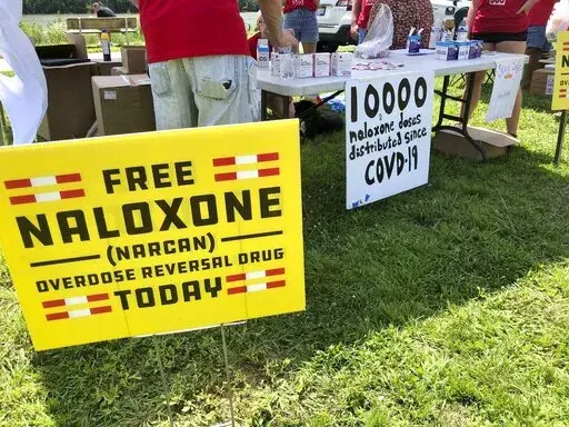 Signs are displayed at a tent during a health event on June 26, 2021, in Charleston, W.Va. Volunteers at the tent passed free doses of naloxone, a drug that reverses the effects of an opioid overdose by helping the person breathe again. The U.S. needs a more nimble strategy and Cabinet-level leadership to counter its festering opioid epidemic, a bipartisan congressional commission said Tuesday. (AP Photo/John Raby, File)