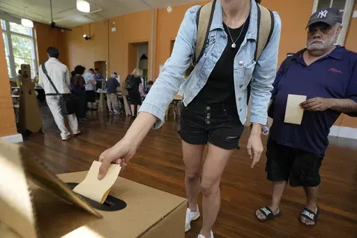 A man, right, waits as a woman drops her ballot into a box a polling place in Redfern as Australians cast their final votes in Sydney, Saturday, Oct. 14, 2023, in their first referendum in a generation that aims to tackle Indigenous disadvantage by enshrining in the constitution a new advocacy committee. Australia will look for new ways to lift Indigenous living standards after voters soundly rejected a proposal to create a new advocacy committee, the deputy prime minister said on Sunday, Oct. 1