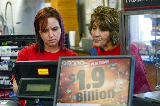 Della Reminar, right, and Crystal Baptiste try to get the ticket machine to scan a card for personal selection numbers for a ticket for the Monday Powerball drawing with an annuity value of at least $1.9 billion, Monday, Nov. 7, 2022, at a convenience store in Renfrew, Pa. (AP Photo/Keith Srakocic)
