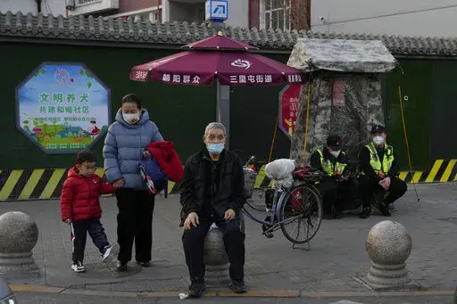 Residents wait to cross a road near members of the Chaoyang militia on duty in Beijing, Monday, March 6, 2023. Chinese economic officials expressed confidence Monday they can meet this year's growth target of "around 5%" by generating 12 million new jobs and encouraging consumer spending following the end of anti-virus controls that kept millions of people at home. (AP Photo/Ng Han Guan)